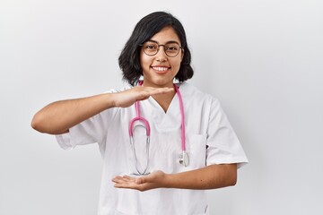 Young hispanic doctor woman wearing stethoscope over isolated background gesturing with hands showing big and large size sign, measure symbol. smiling looking at the camera. measuring concept.