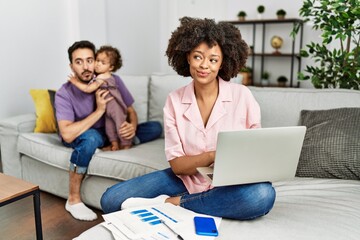 Mother of interracial family working using computer laptop at home smiling looking to the side and staring away thinking.