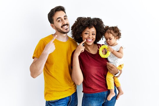 Interracial young family of black mother and hispanic father with daughter smiling cheerful showing and pointing with fingers teeth and mouth. dental health concept.
