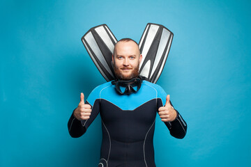 Happy diver with fins showing thumb up gesture on blue background