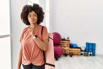 African american woman with afro hair holding yoga mat at pilates room thinking concentrated about...