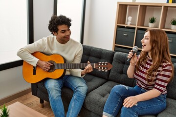 Young couple playing classical guitar and singing using microphone at home.