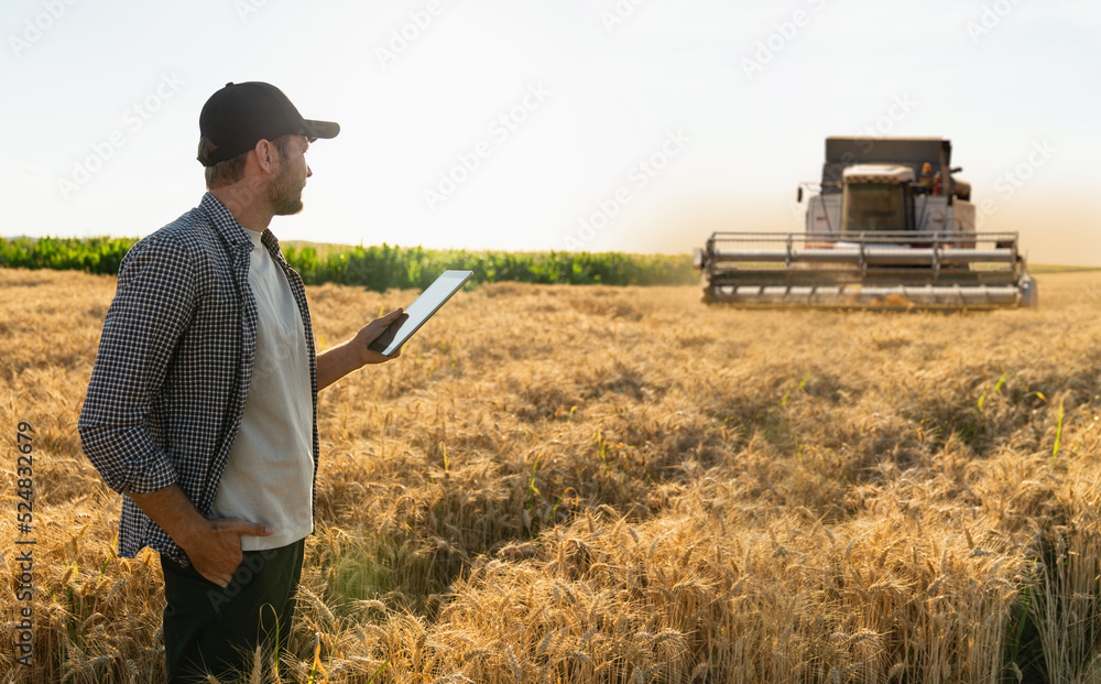 Poster farmer with digital tablet on a background of combine harvester. smart farming concept.