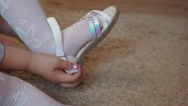 a little girl put on sandals,the little girl put on her sandals on the carpet by herself