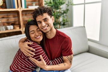 Young latin couple smiling happy and hugging sitting on the sofa at home.