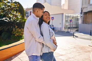 Young latin couple expecting baby hugging each other standing at park