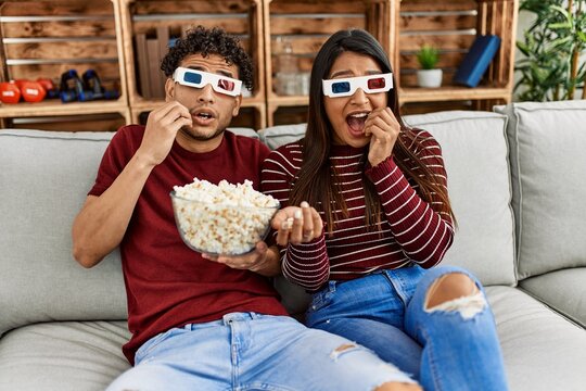 Young latin couple scared watching movie using 3d glasses at home.