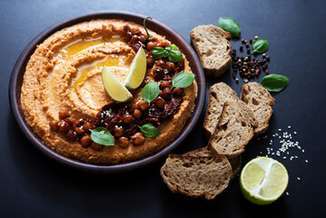 Hummus with sun-dried tomatoes on a brown plate. Healthy and delicious food