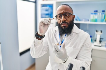 Fototapeta premium Young african american man wearing scientist uniform using tweezer at laboratory