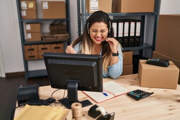 Young hispanic woman working at small business ecommerce wearing headset screaming proud, celebrating victory and success very excited with raised arm