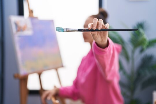 Young woman artist smiling confident holding paintbrush at art studio
