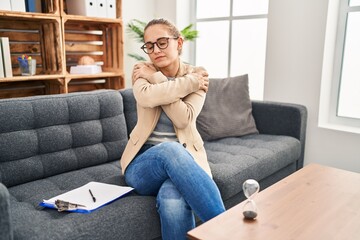 Obraz premium Young woman working at consultation office hugging oneself happy and positive, smiling confident. self love and self care