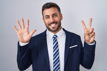 Handsome hispanic man wearing suit and tie showing and pointing up with fingers number seven while smiling confident and happy.