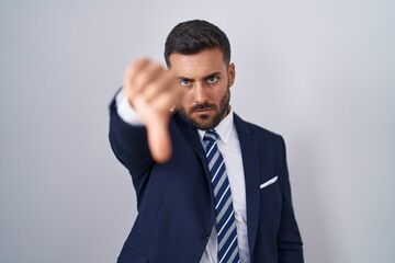 Handsome hispanic man wearing suit and tie looking unhappy and angry showing rejection and negative with thumbs down gesture. bad expression.