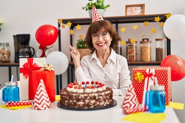Middle age woman celebrating birthday holding big chocolate cake smiling happy pointing with hand and finger to the side