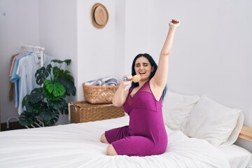 Young caucasian woman singing song using brush as a microphone at bedroom