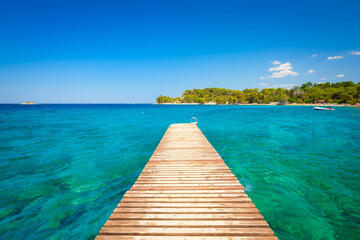 Pier at sea in the summertime.  Azure sea and shore with rocks. Clear sea water and clear sky. Adriatic Sea, Croatia.