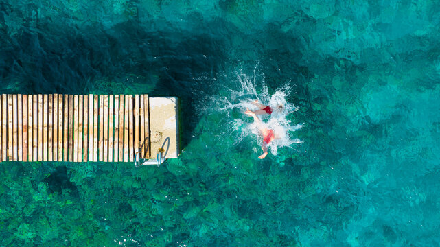 A carefree couple jumps into the azure sea. Aerial view. A vacation in the summertime. Young and energetic people dive into the water together. A fun vacation at the sea together.