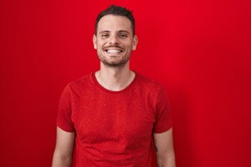 Young hispanic man standing over red background with a happy and cool smile on face. lucky person.