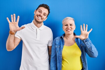 Young brazilian mother and son standing over blue background showing and pointing up with fingers number ten while smiling confident and happy.