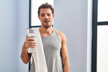 Young hispanic man wearing sportswear drinking water looking sleepy and tired, exhausted for...