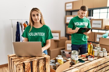 Young woman and man wearing volunteer t shirt at donations stand thinking attitude and sober expression looking self confident