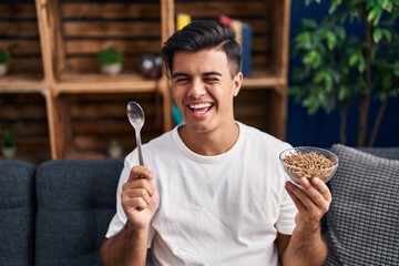 Hispanic man eating healthy whole grain cereals with spoon winking looking at the camera with sexy...
