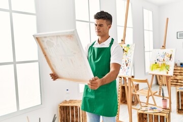 Young hispanic man looking draw canvas at art studio