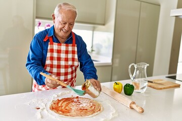 Senior man smiling confident cooking pizza at kitchen