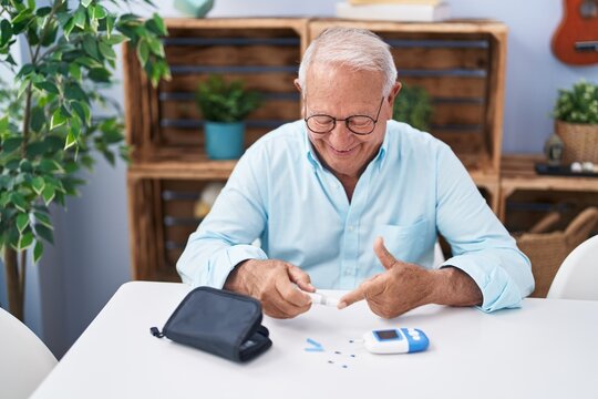 Senior grey-haired man measuring glucose sitting on table at home