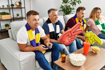 Group of middle age friends watching and supporting soccer match using smartphone at home.