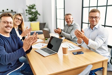 Group of middle age business workers smiling happy. Sitting on the table clapping and looking to the camera at the office.