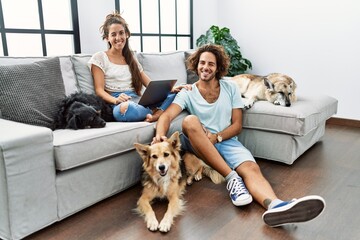 Young hispanic couple with dogs relaxing at home winking looking at the camera with sexy expression, cheerful and happy face.