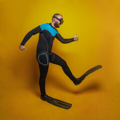 Fototapeta na wymiar Traveling concept. Happy diver in a mask and fins going somewhere against yellow studio background