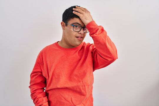 Young hispanic man with down syndrome standing over white background surprised with hand on head for mistake, remember error. forgot, bad memory concept.