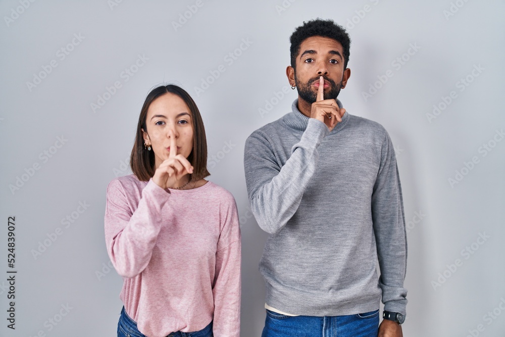 Poster Young hispanic couple standing together asking to be quiet with finger on lips. silence and secret concept.