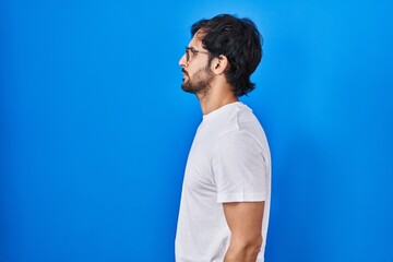 Fototapeta na wymiar Handsome latin man standing over blue background looking to side, relax profile pose with natural face with confident smile.