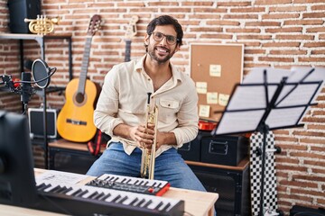 Young hispanic man musician holding trumpet at music studio