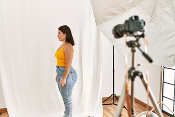 Young beautiful hispanic woman posing as model at photography studio looking to side, relax profile...