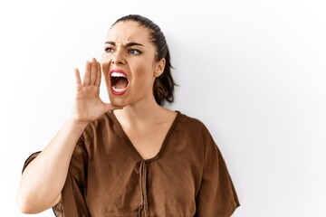 Young brunette woman standing over isolated background shouting and screaming loud to side with hand on mouth. communication concept.