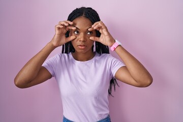 African american woman with braids standing over pink background trying to open eyes with fingers, sleepy and tired for morning fatigue