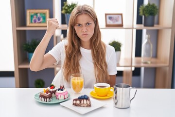 Obraz na płótnie Canvas Young caucasian woman eating pastries t for breakfast angry and mad raising fist frustrated and furious while shouting with anger. rage and aggressive concept.