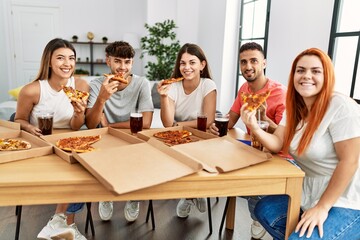 Group of young people smiling happy eating italian pizza sitting on the table at home