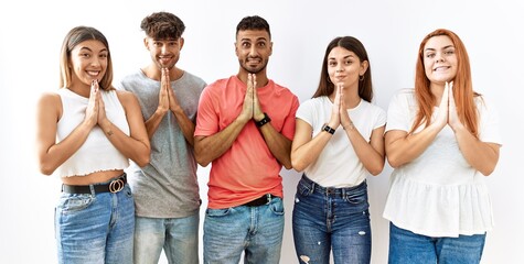 Obraz premium Group of young friends standing together over isolated background praying with hands together asking for forgiveness smiling confident.