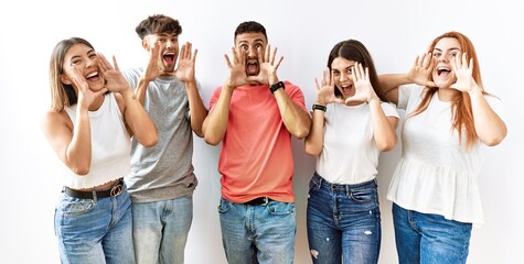 Group of young friends standing together over isolated background smiling cheerful playing peek a boo with hands showing face. surprised and exited