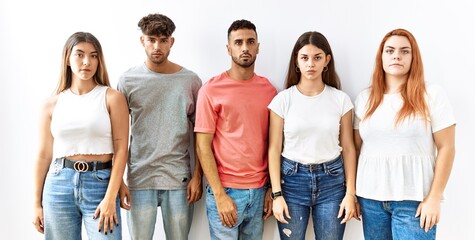 Group of young friends standing together over isolated background relaxed with serious expression on face. simple and natural looking at the camera.