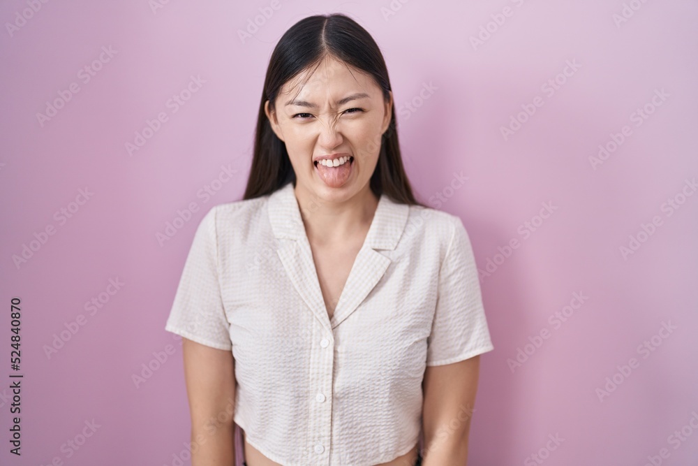 Sticker chinese young woman standing over pink background sticking tongue out happy with funny expression. e