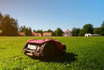 Red robotic lawn mower mows the grass on the lawn.