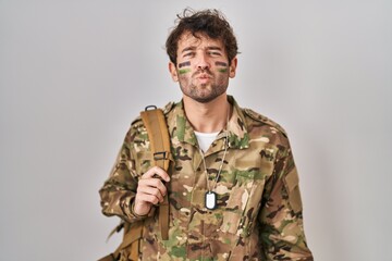 Hispanic young man wearing camouflage army uniform looking at the camera blowing a kiss on air being lovely and sexy. love expression.