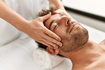 Young hispanic man having facial massage at beauty center